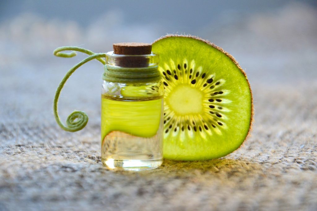 Imagem de um pequeno frasco de vidro contendo óleo essencial. Ao lado dele um pedaço de kiwi cortado em rodela.
