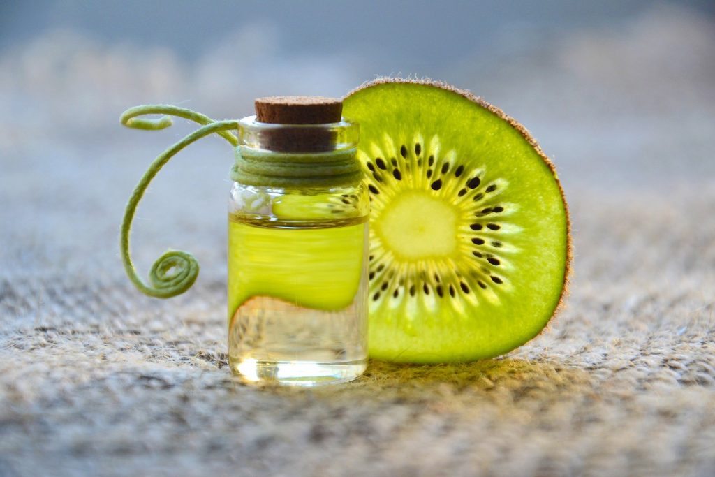 Imagem de um pequeno frasco de vidro contendo óleo essencial. Ao lado dele um pedaço de kiwi cortado em rodela.