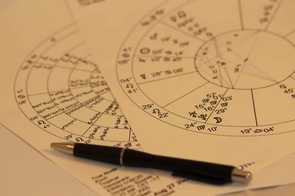 Imagem de duas folhas de papel sobre uma mesa onde está desenhado um mapa astral. Sobre eles, uma caneta de ponta grossa.