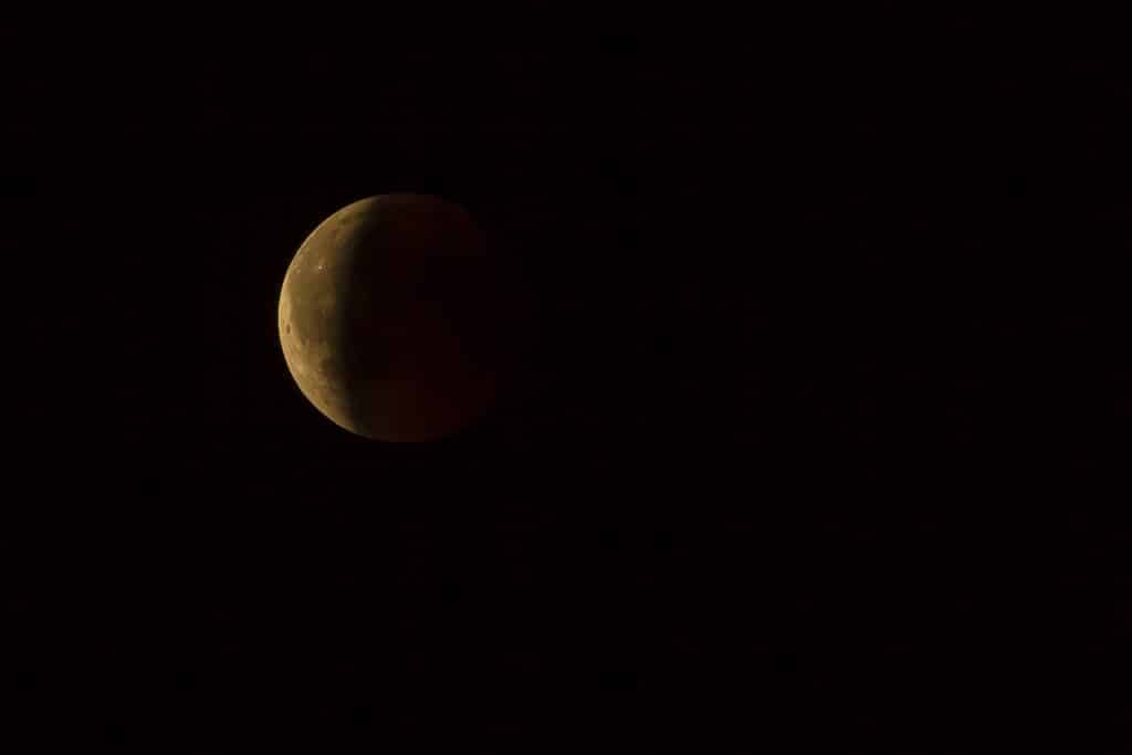 Imagem do céu noturno, sem estrelas e ao fundo um eclipse lunar total.