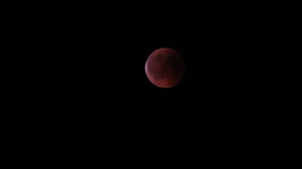 Imagem com a lua ao fundo e o eclipse lunar total.