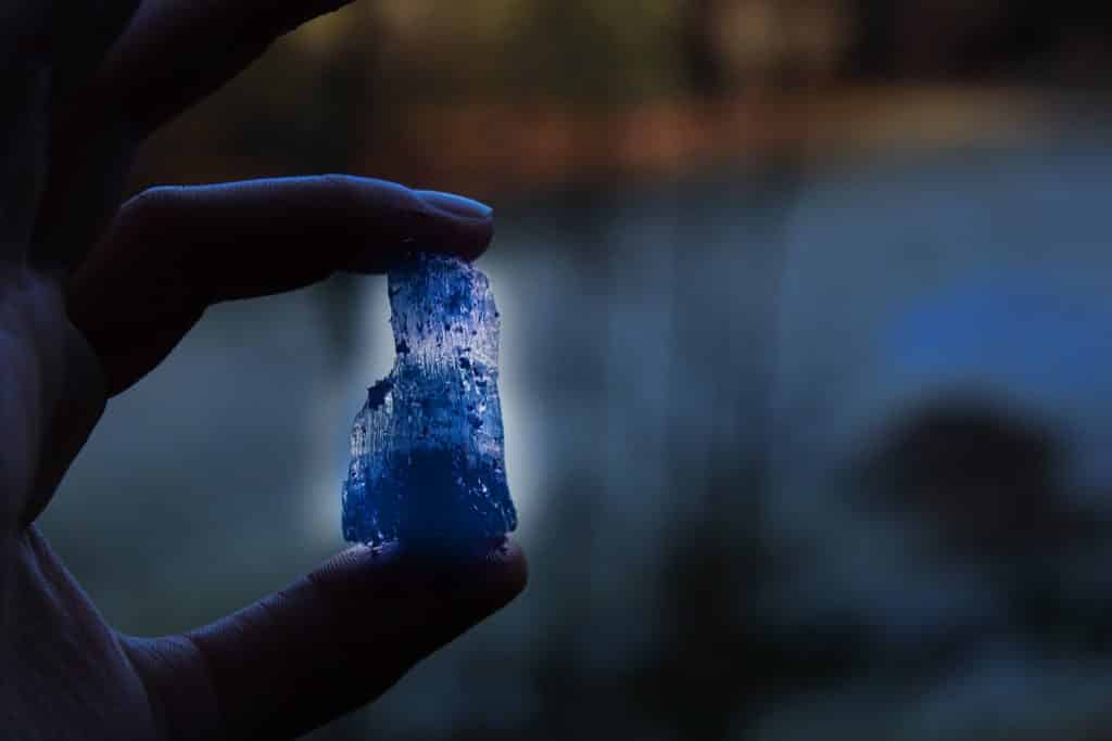 Imagem de uma mão feminina segurando um cristal de água-marinha na cor azul.
