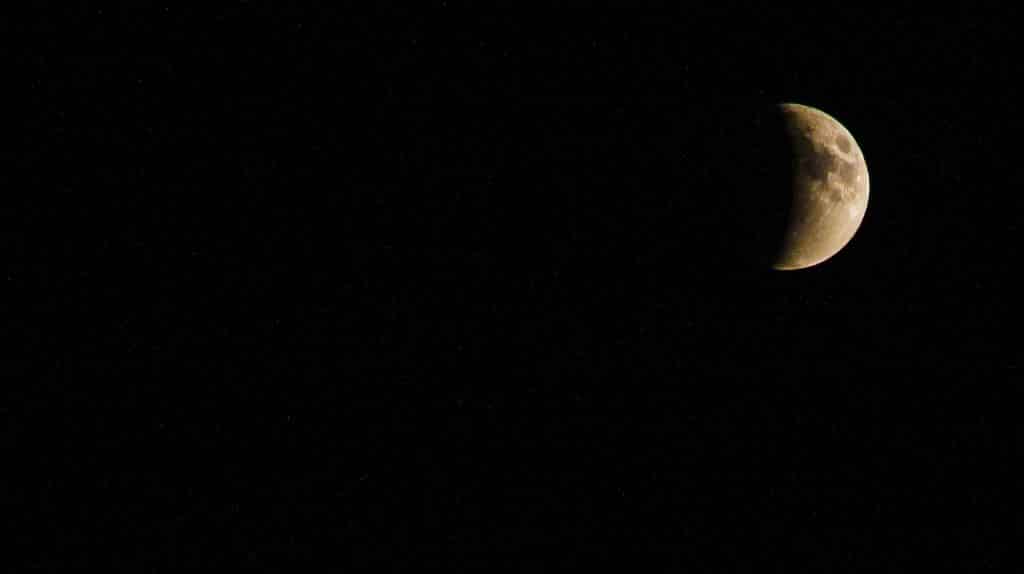 Imagem de um céu estrelado e ao fundo a lua e seu eclipse lunar total.
