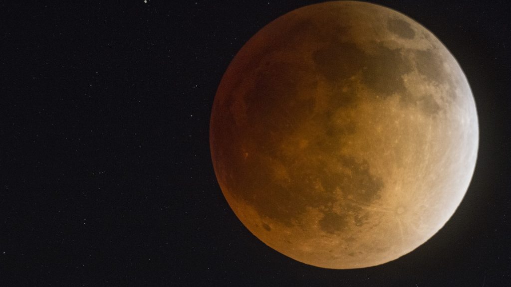 Imagem de uma super lua e ao fundo o céu estrelado.
