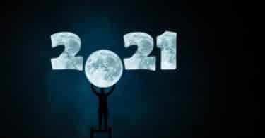 Imagem do ano 2021 desenhando com o fundo da cor da lua. O número zero do ano 2021 está em formato de lua cheia. Um homem está em cima de uma escada e com as mãos segura o número zero em formato de lua.
