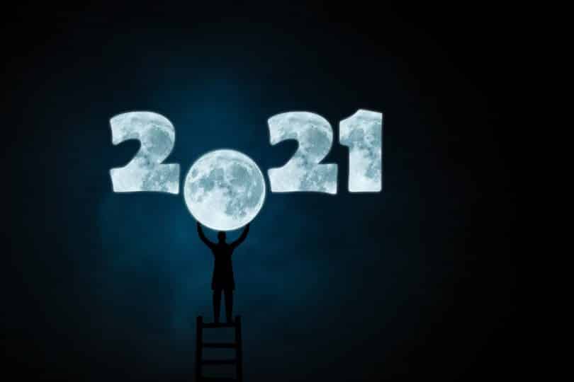 Imagem do ano 2021 desenhando com o fundo da cor da lua. O número zero do ano 2021 está em formato de lua cheia. Um homem está em cima de uma escada e com as mãos segura o número zero em formato de lua.