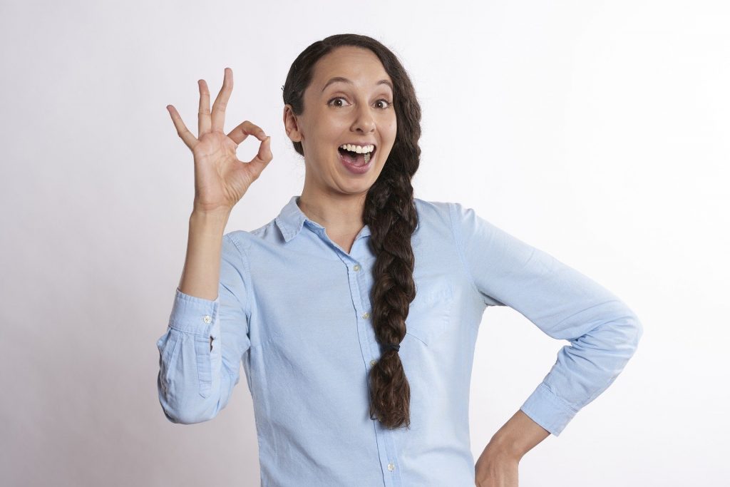 Imagem de uma mulher feliz e dando um ok com uma de suas mãos, confirmando que pessoas que acreditam em signos são mais felizes.