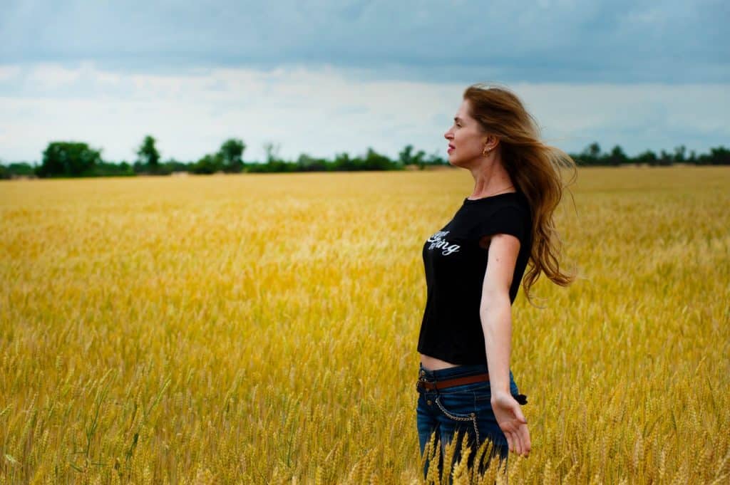 Mulher branca de braços abertos num campo.