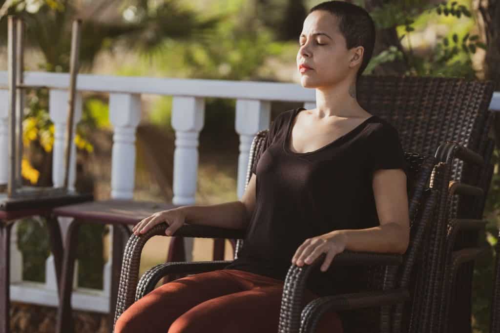 Mulher sentada em uma cadeira ao ar livre com os olhos fechados meditando.