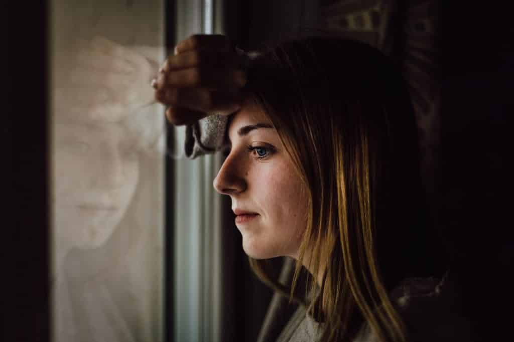 Mulher encara o próprio reflexo na janela.