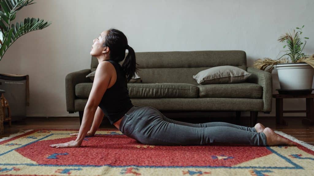 Mulher asiática se alongando no chão de uma sala.