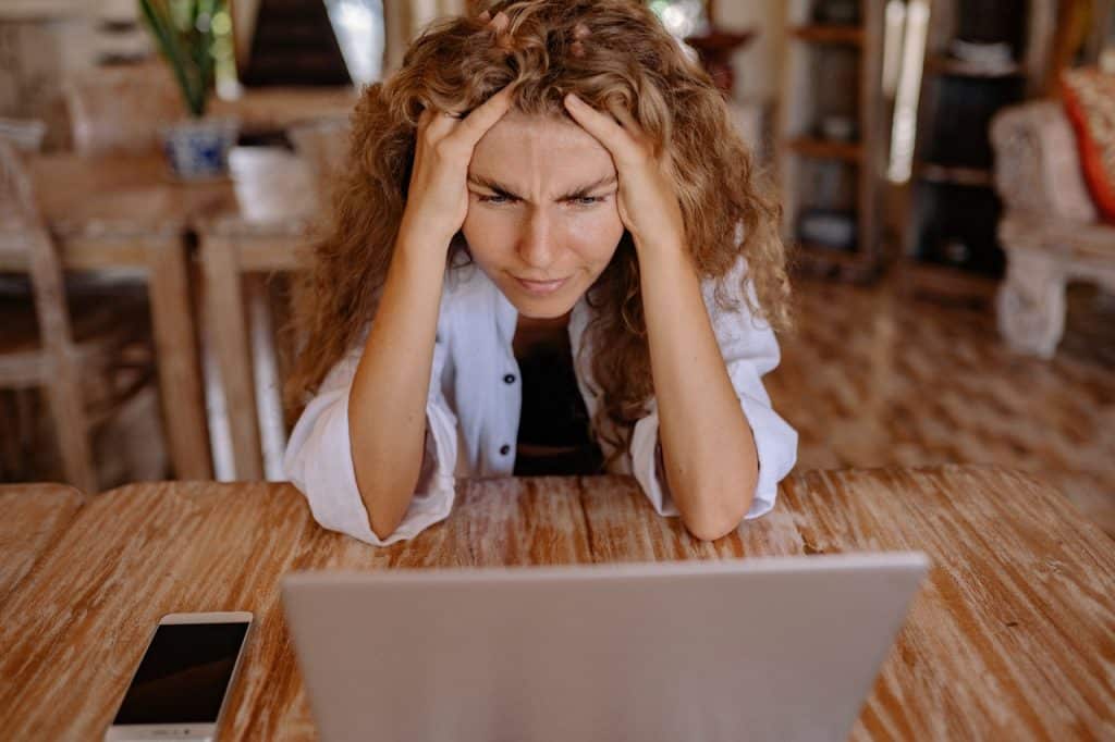 Mulher irritada com as mãos na cabeça olhando para o notebook.