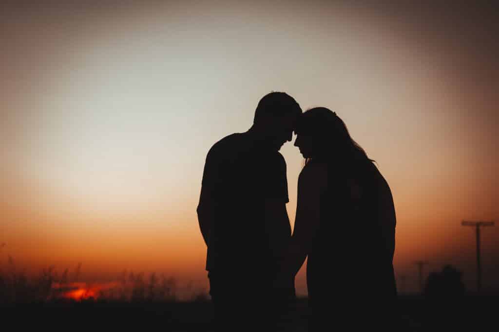 Imagem de fundo com um lindo por do sol e em destaque a silhueta de um lindo casal de mãos dadas.