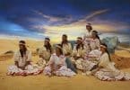Imagem de oito mulheres indígenas em um terreiro dentro de sua tribo. Elas usam cabelos longos e soltos e uma faixa decorativa na cabeça. Também usam vestidos longos, na cor bege com detalhes na cor vermelha. Todos os vestidos são iguais.