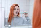 Imagem de uma mulher ruiva no banheiro escovando os dentes que estavam estragados.