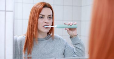 Imagem de uma mulher ruiva no banheiro escovando os dentes que estavam estragados.