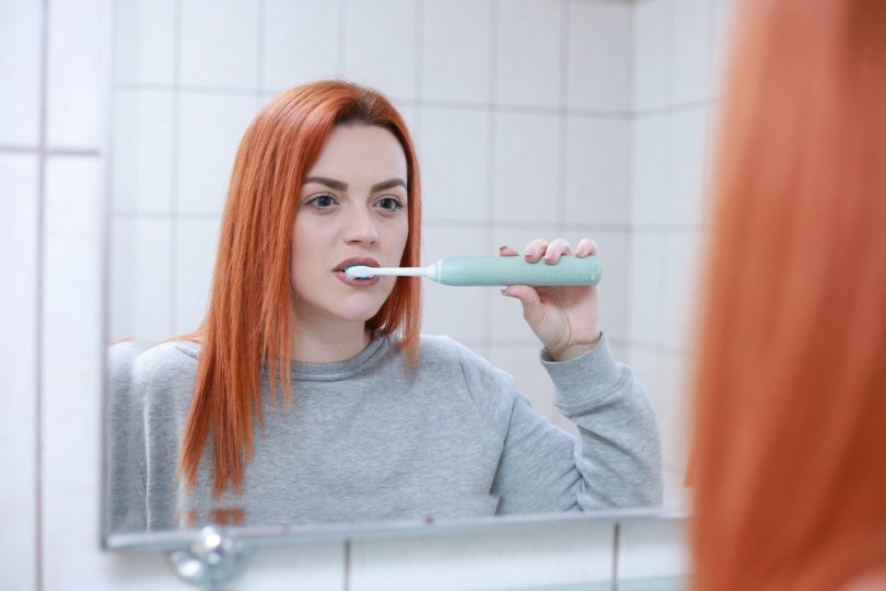 Imagem de uma mulher ruiva no banheiro escovando os dentes que estavam estragados.