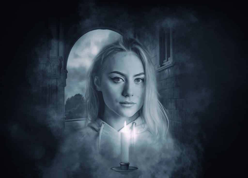 Imagem preta e branco de uma assombração mulher segurando uma vela acesa em suas mãos.