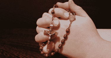 Mãos unidas rezando enquanto seguram um terço