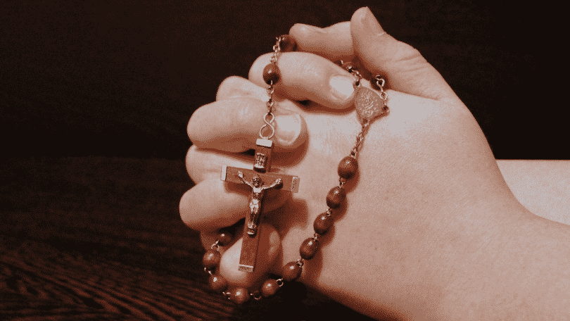 Mãos unidas rezando enquanto seguram um terço