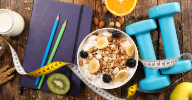 Foto representativa de uma dieta com banana e aveia em um pote ao lado de pesos, fita métrica e lápis