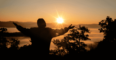 Silhueta de homem agradecendo com os braços erguidos durante por do sol