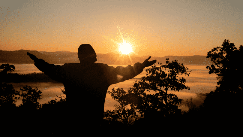 Silhueta de homem agradecendo com os braços erguidos durante por do sol