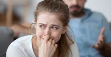 Mulher branca chorando com expressão triste, e homem branco atrás.