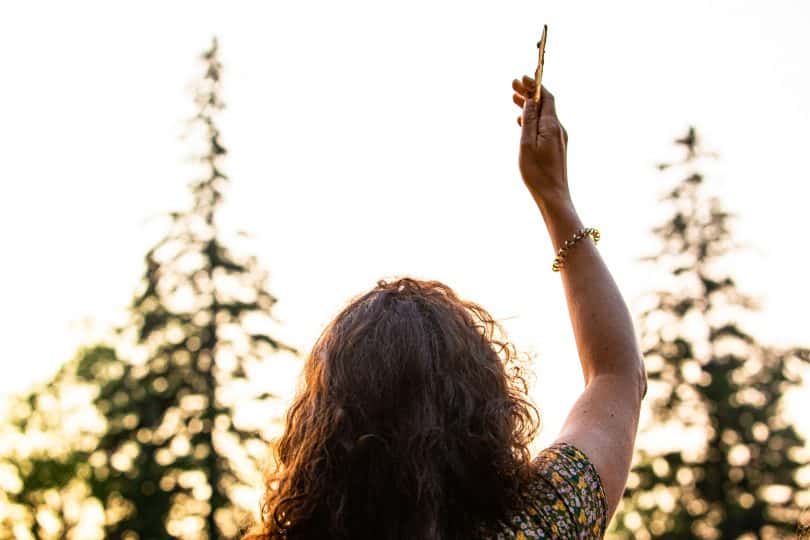 Mulher com a mão pra cima de frente para árvores