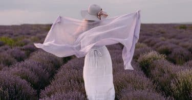 Mulher de costas usando vestido e lenço brancos, num campo de lavandas.