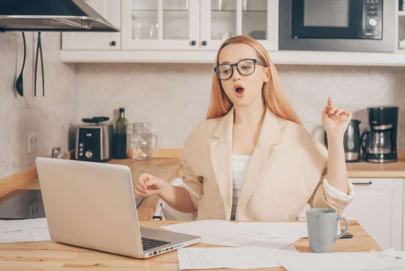 Mulher branca trabalhando com computador na cozinha.