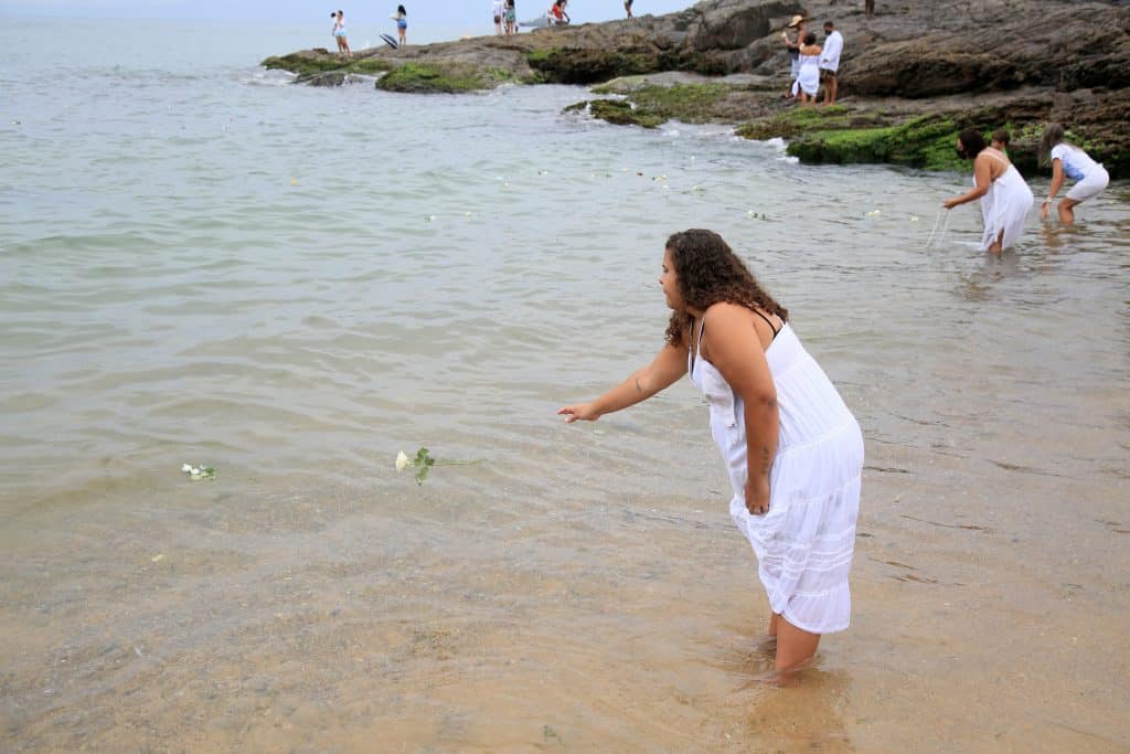 Imagem do mar e várias pessoas, homens e mulheres integrantes do Candomblé, na água se preparando para o banho de Iemanjá.