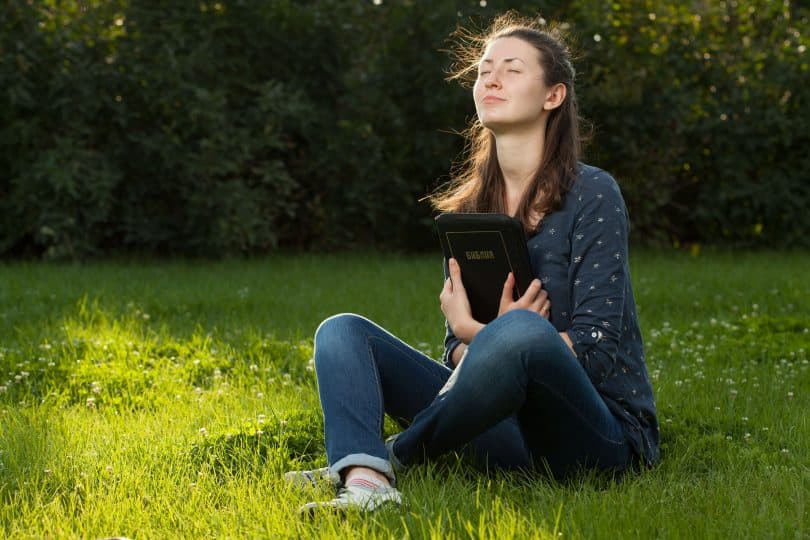 Mulher sentada sobre grama. Ela está segurando uma bíblia.