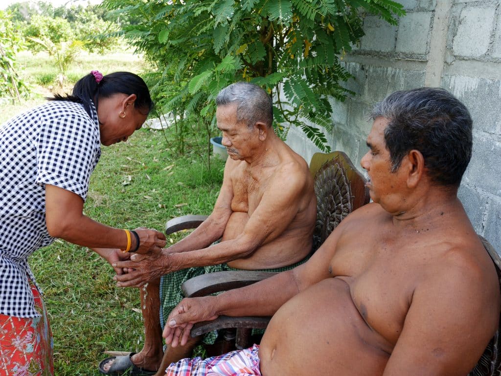 Imagem de uma senhora benzedeira fazendo um benzimento em dois senhores sentados.
