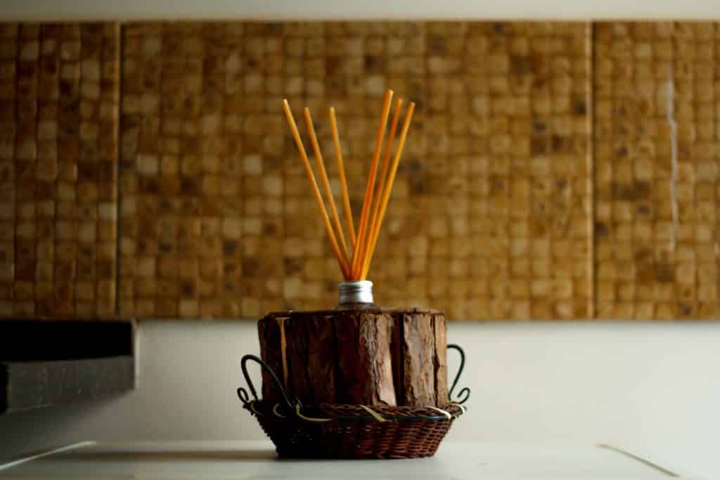 Imagem de vários palitos de incensos dispostos em um grande incensário de madeira colocado sobre uma mesa de fundo branco.