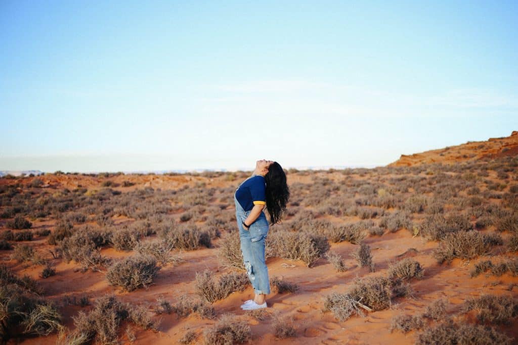 Mulher branca olhando para cima num deserto.