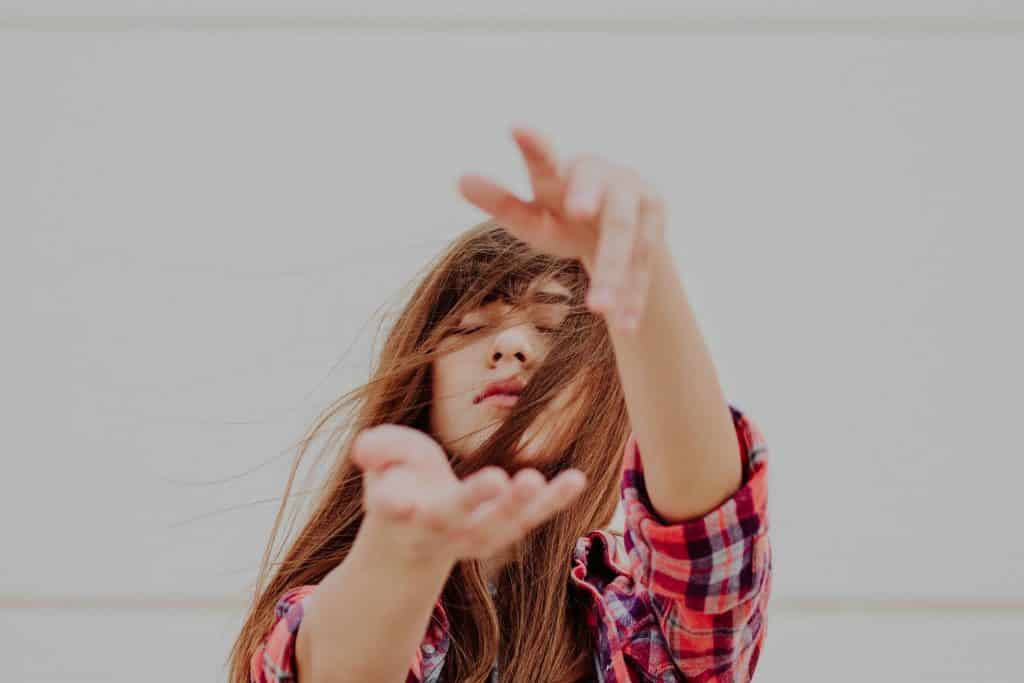 Mulher branca e ruiva com os olhos fechados e mãos a frente do corpo.