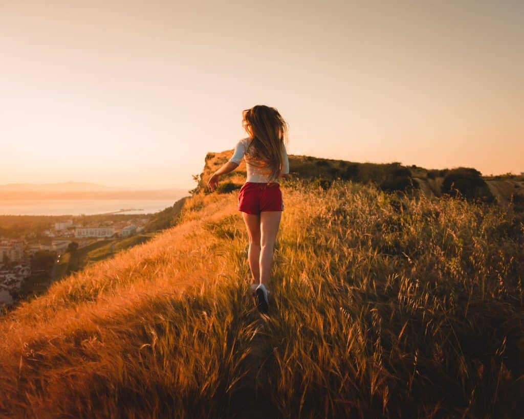 Mulher branca de costas correndo num morro.