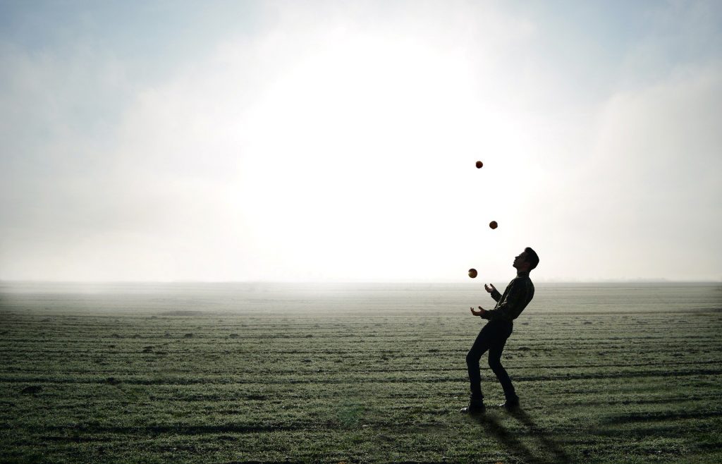 Imagem de um homem equilibrando três bolas. Ele joga ao alto as três bolas e faz o equilíbrio delas com as duas mãos.
