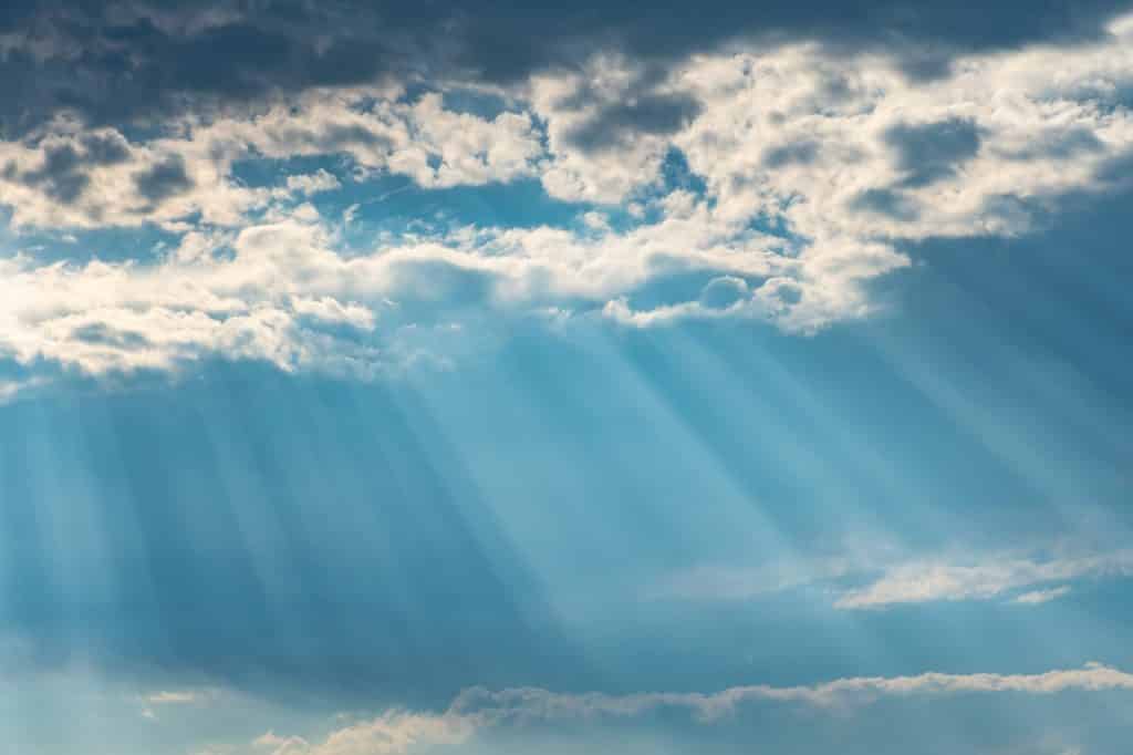 Sob céu azul, nuvens e raios solares.