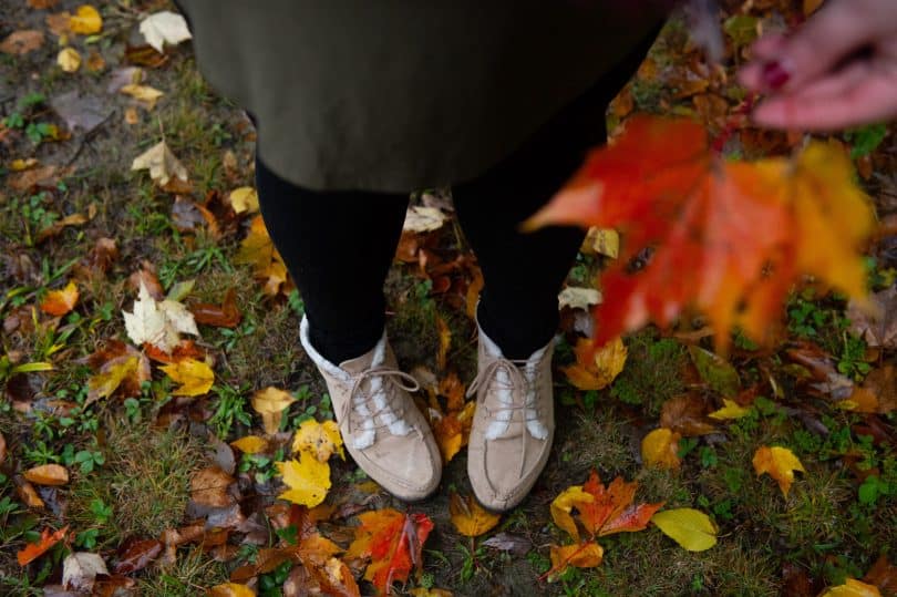 Pés de alguém em um gramado com folhas de outono