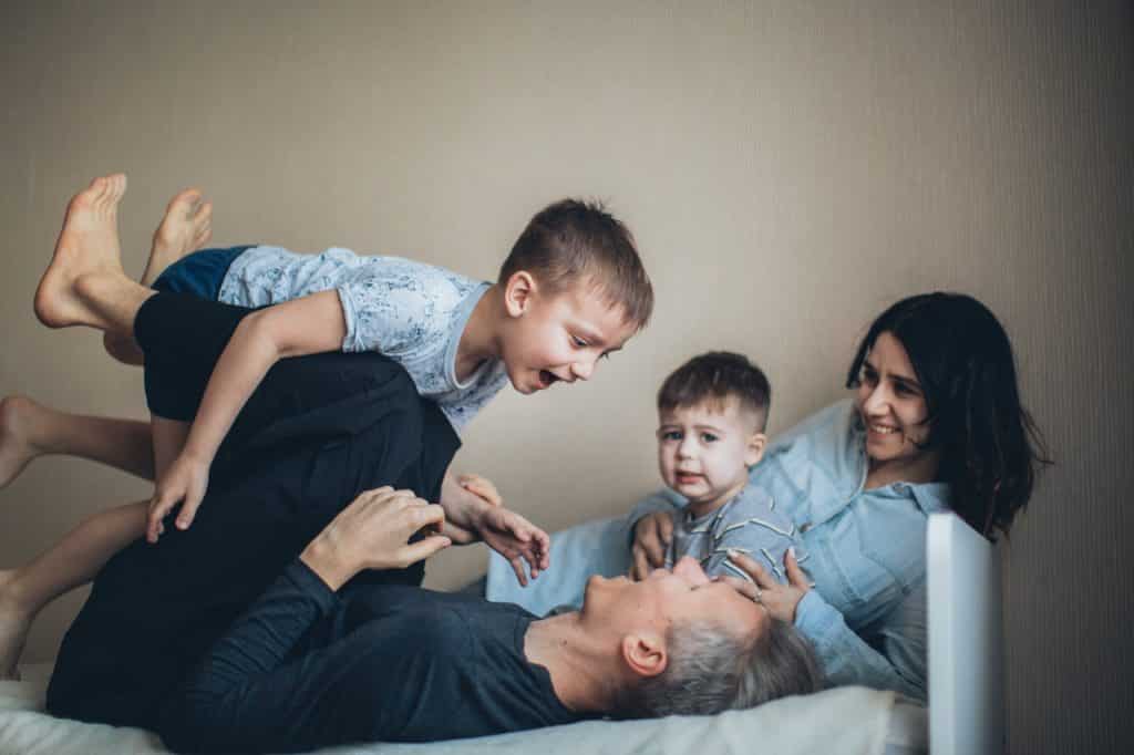 Pais brincando com os dois filhos pequenos no sofá.