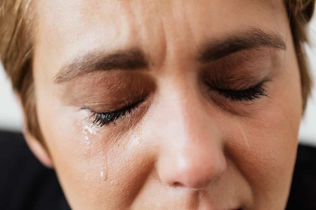 Recorte de uma mulher de olhos fechados escorrendo lágrimas no rosto. 