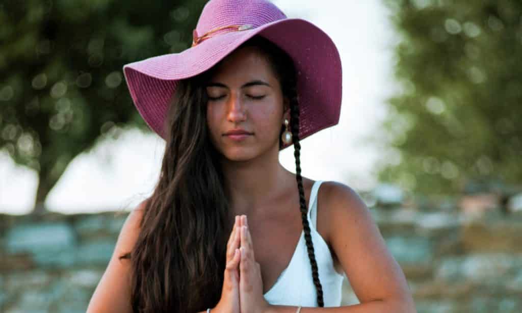 Mulher com os olhos fechados e mãos unidas próximas do corpo. 