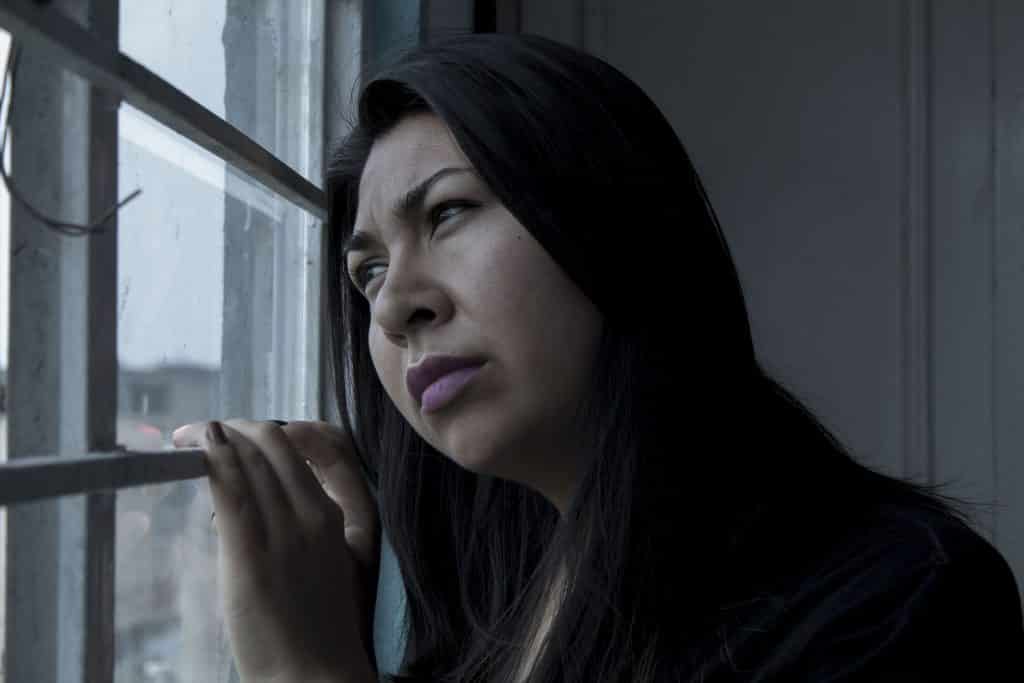 Imagem de uma mulher triste olhando pela janela. ELa está com a cabeça encostada na janela. Está se sentindo culpada por ter feito algo. Ela usa cabelos longos.