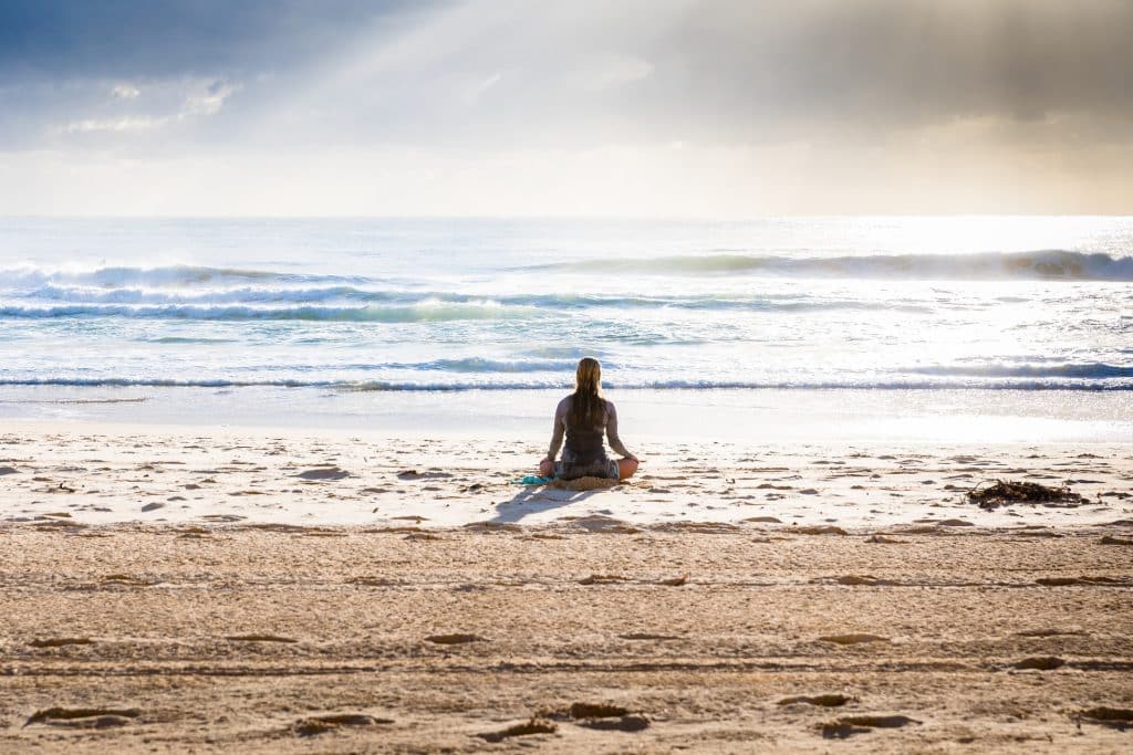 Mulher branca meditando na praia.