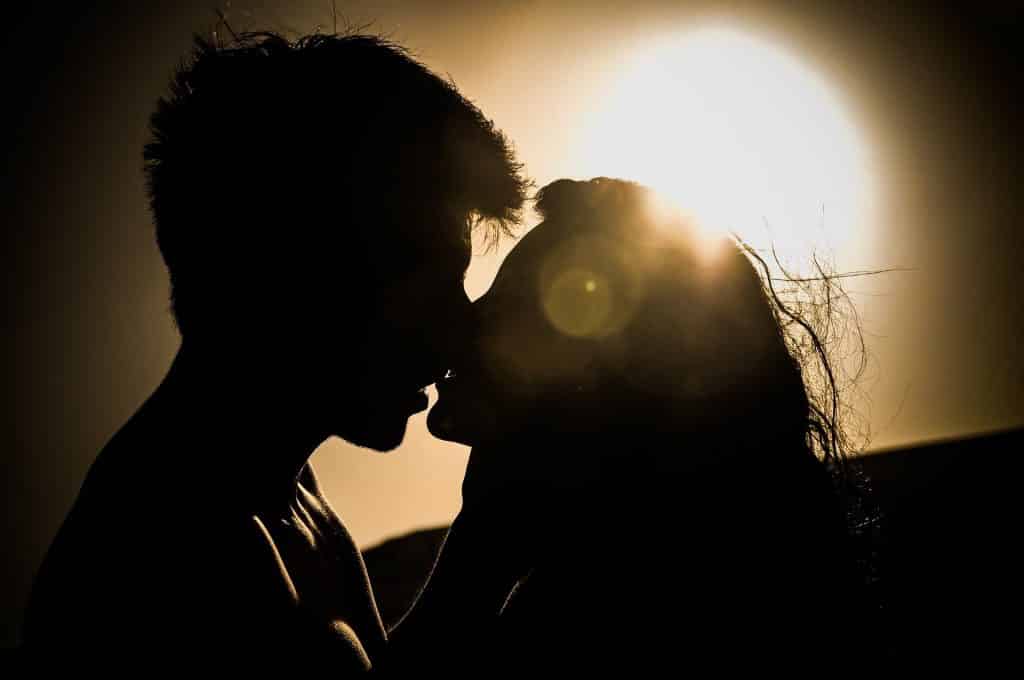 Imagem de um casal se beijando e ao fundo um lindo pôr do sol.