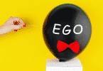 Balão escrito "ego" prestes a ser furado por um palito de dente
