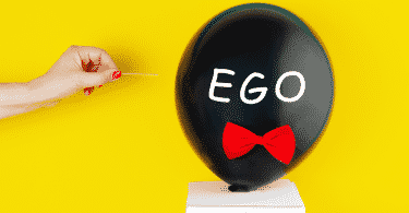 Balão escrito "ego" prestes a ser furado por um palito de dente