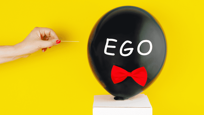 Balão escrito "ego" prestes a ser furado por um palito de dente